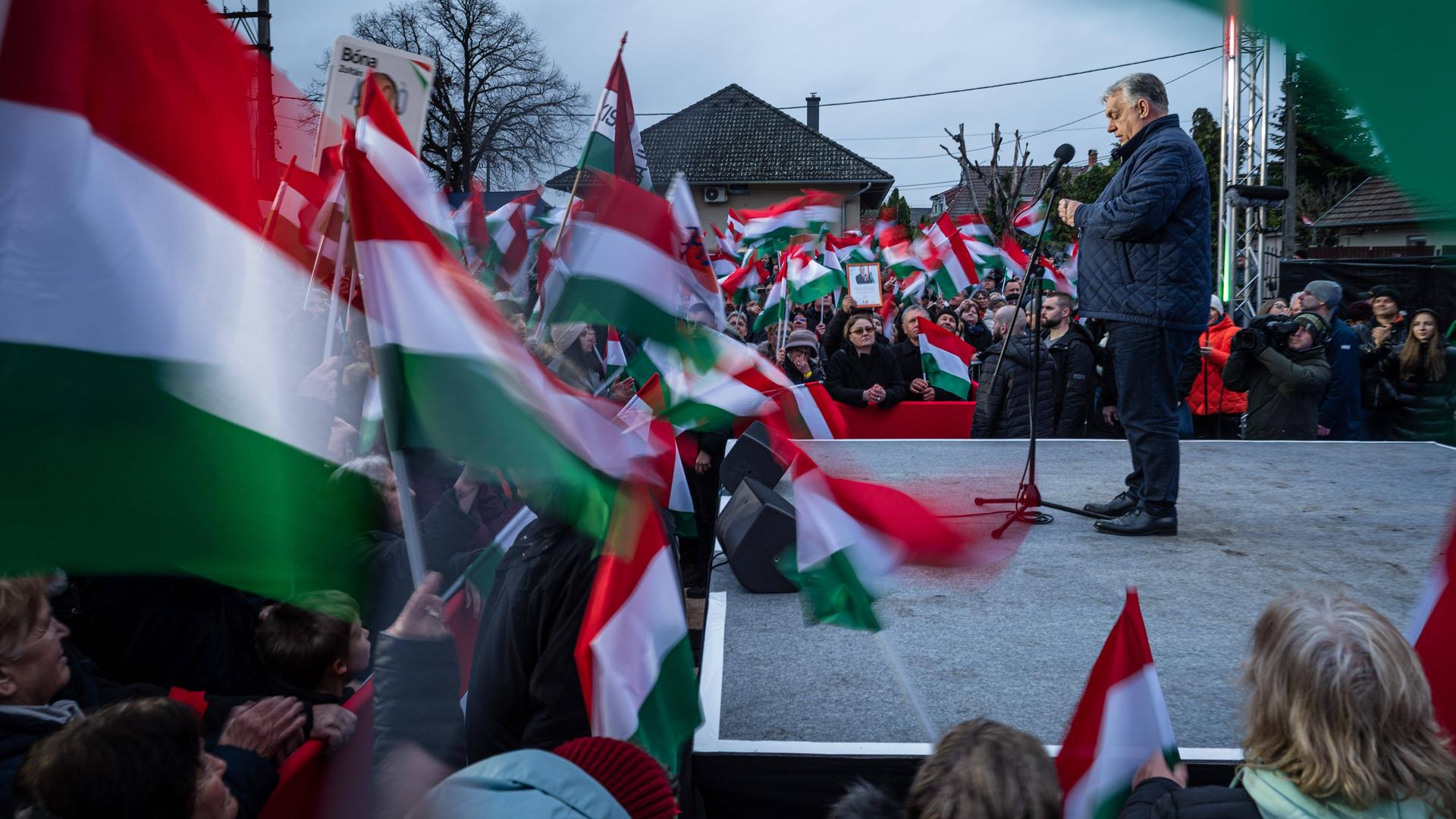 Ungarns Ministerpräsident Viktor Orbán steht auf einer Bühne während einer Wahlkampfveranstaltung. Es sind viele ungarische Fahnen zu sehen. 