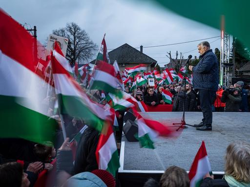 Ungarns Ministerpräsident Viktor Orbán steht auf einer Bühne während einer Wahlkampfveranstaltung. Es sind viele ungarische Fahnen zu sehen. 
