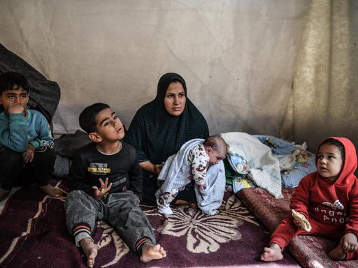 Eine Frau mit Kopftuch sitzt mit ihren Kindern in einem Zelt.