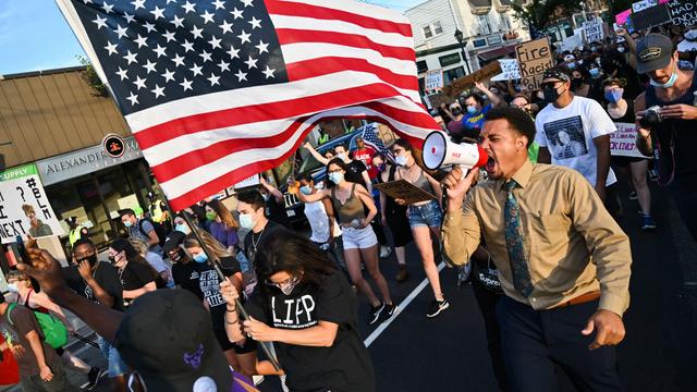 Demonstranten während einer Black-Lives-Matter-Demonstration tragen eine amerikanische Flagge und schreien wütend in ein Megafon.