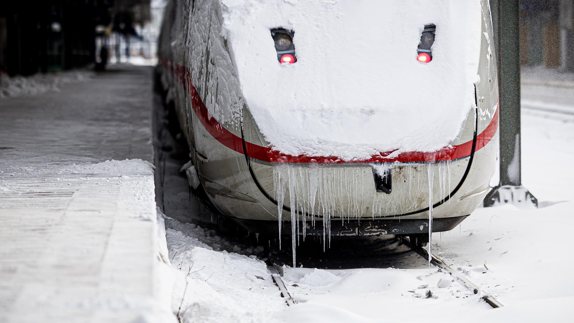 Rückansicht eines ICE-Zuges, dessen Scheibe verschneit ist. Lange Eiszapfen reichen bis auf die Schienen.