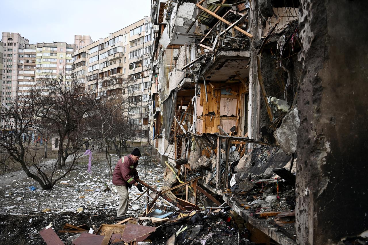 Ein Mann räumt Trümmer vor einem zerstörten mehrstöckigen Wohnhaus weg.