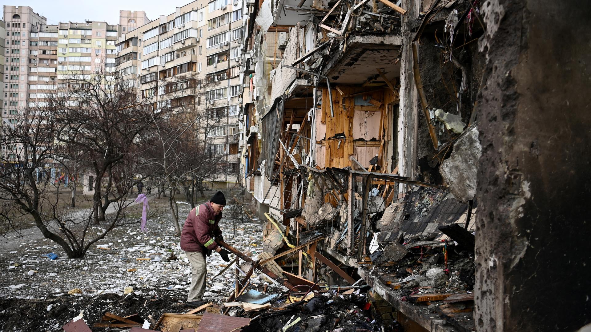 Ein Mann räumt Trümmer vor einem zerstörten mehrstöckigen Wohnhaus weg.