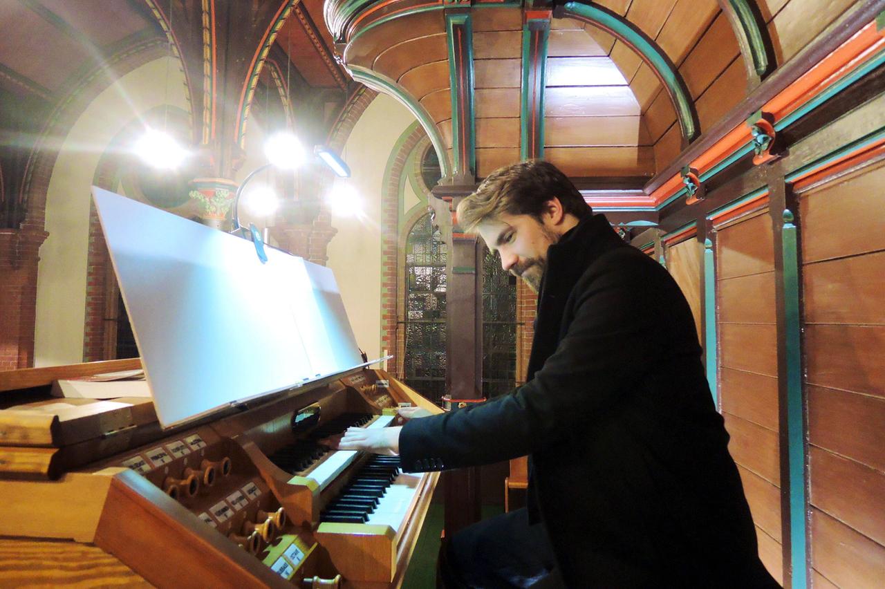 Der englische Jazz-Keyboarder Kit Downes sitzt lächelnd an einer Orgel, während er in einem dicken, schwarzen Mantel spielt. 