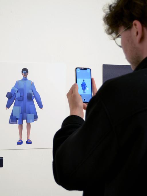 Ein Besucher der Ausstellung "virtuelles Beiwerk" steht mit dem Smartphone vor einem Ausstellungsstück.