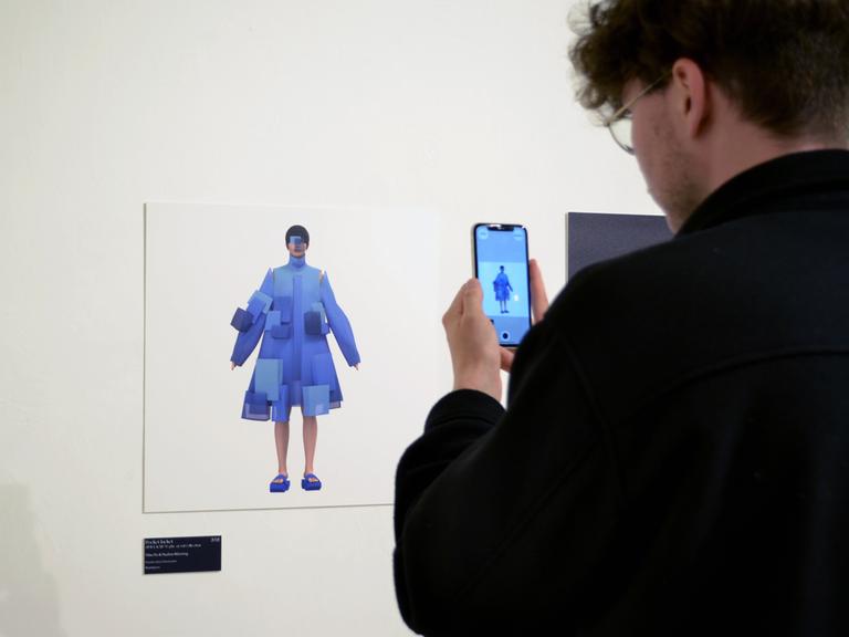 Ein Besucher der Ausstellung "virtuelles Beiwerk" steht mit dem Smartphone vor einem Ausstellungsstück.