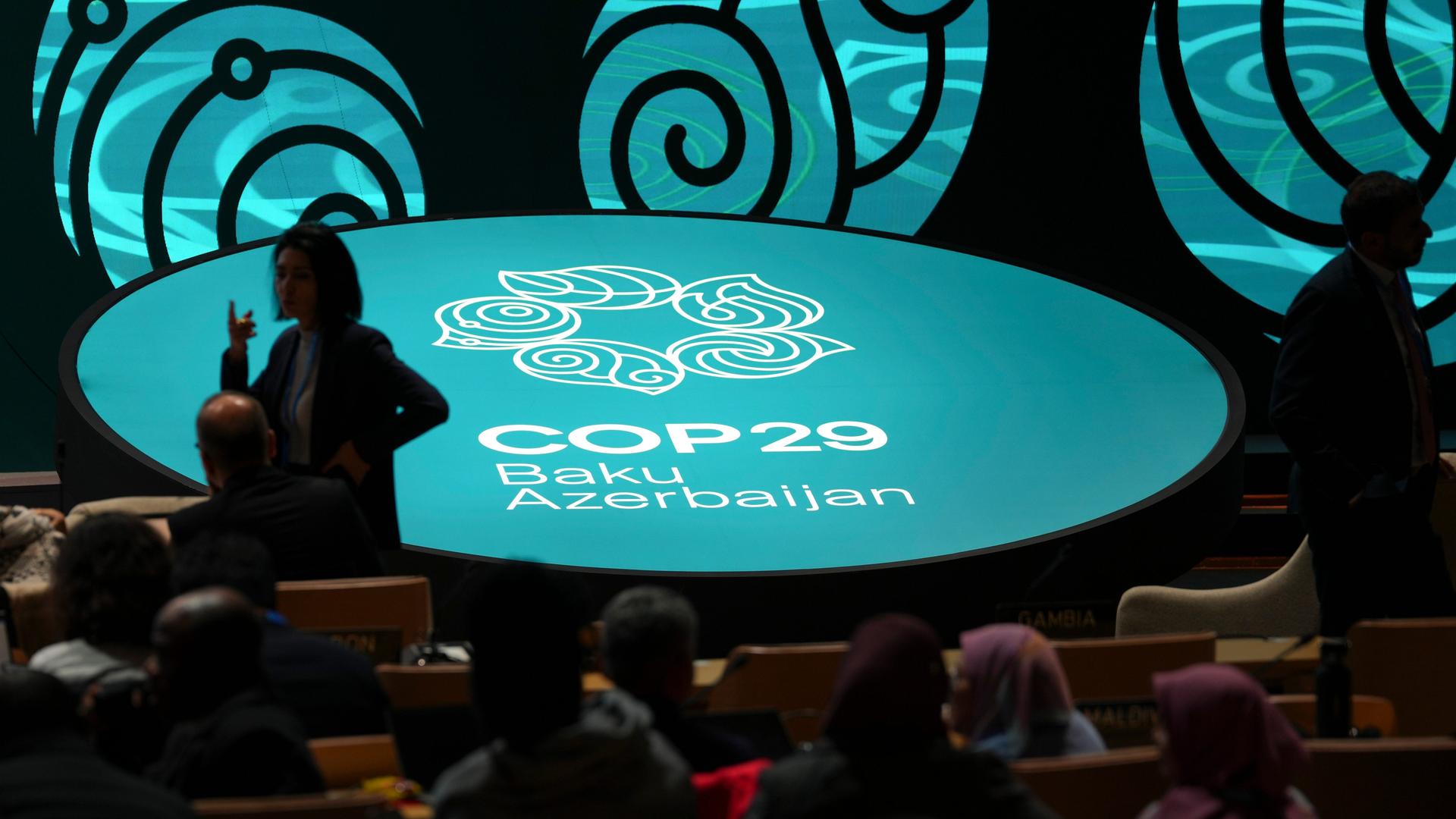 Das Logo der Klimakonferenz in Baku leuchtet türkis in einem dunklem Raum.