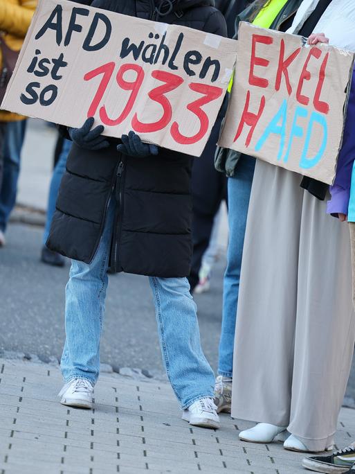 Teilnehmer einer Protestveranstaltung gegen eine AfD-Demonstration halten Schilder "AfD wählen ist so 1993" und "Ekelhafd".