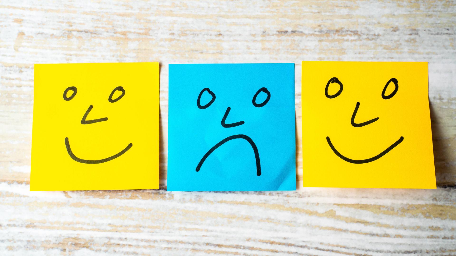 Mentale Gesundheit Konzept, gelbe Haftnotizen mit glücklichen gesichtern und eine blaue Haftnotiz mit einem traurigen Gesicht