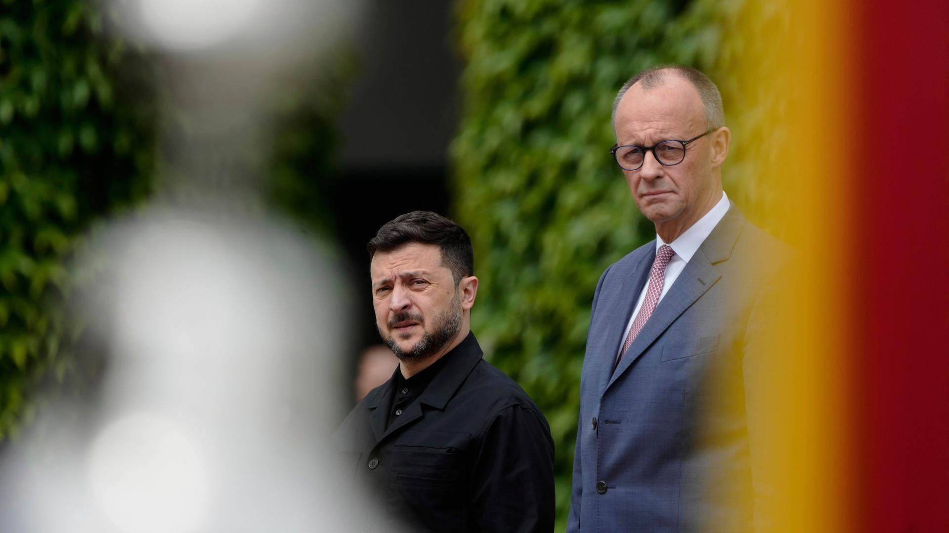 Bundeskanzler Friedrich Merz (rechts) steht im Freien vor einer grünen Hecke, er ist im Halbprofil zu sehen. Von Merz aus gesehen rechts steht Wolodymyr Selenskyj. Bundeskanzler Friedrich Merz (rechts) steht im Freien vor einer grünen Hecke, er ist im Halbprofil zu sehen. Von Merz aus gesehen rechts steht Wolodymyr Selenskyj.