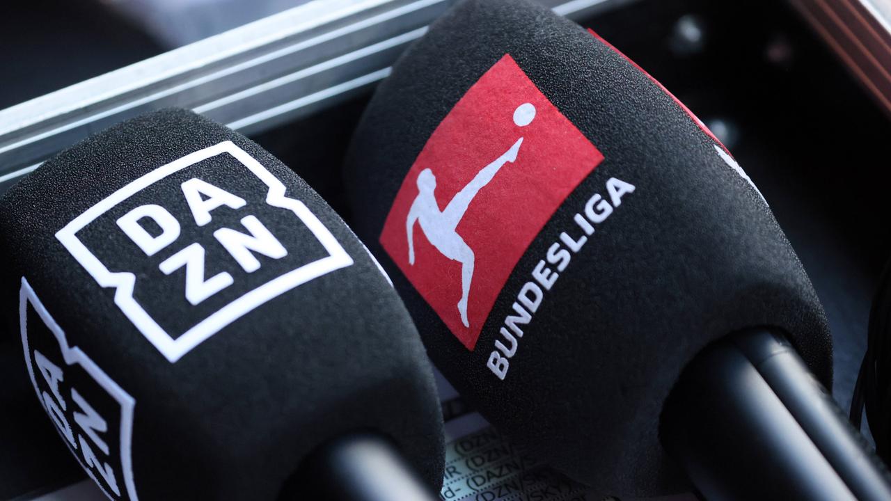 Mikrofone mit den Logos von DAZN und der Bundesliga liegen nebeneinander.