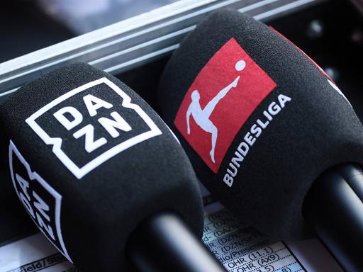 Mikrofone mit den Logos von DAZN und der Bundesliga liegen nebeneinander.