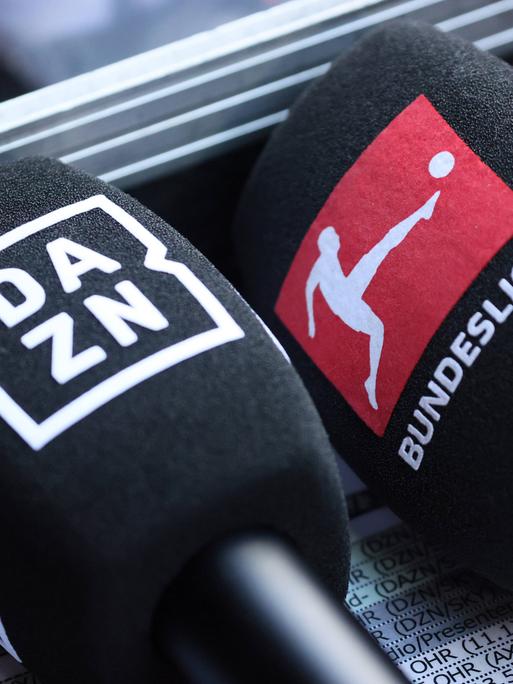 Mikrofone mit den Logos von DAZN und der Bundesliga liegen nebeneinander.