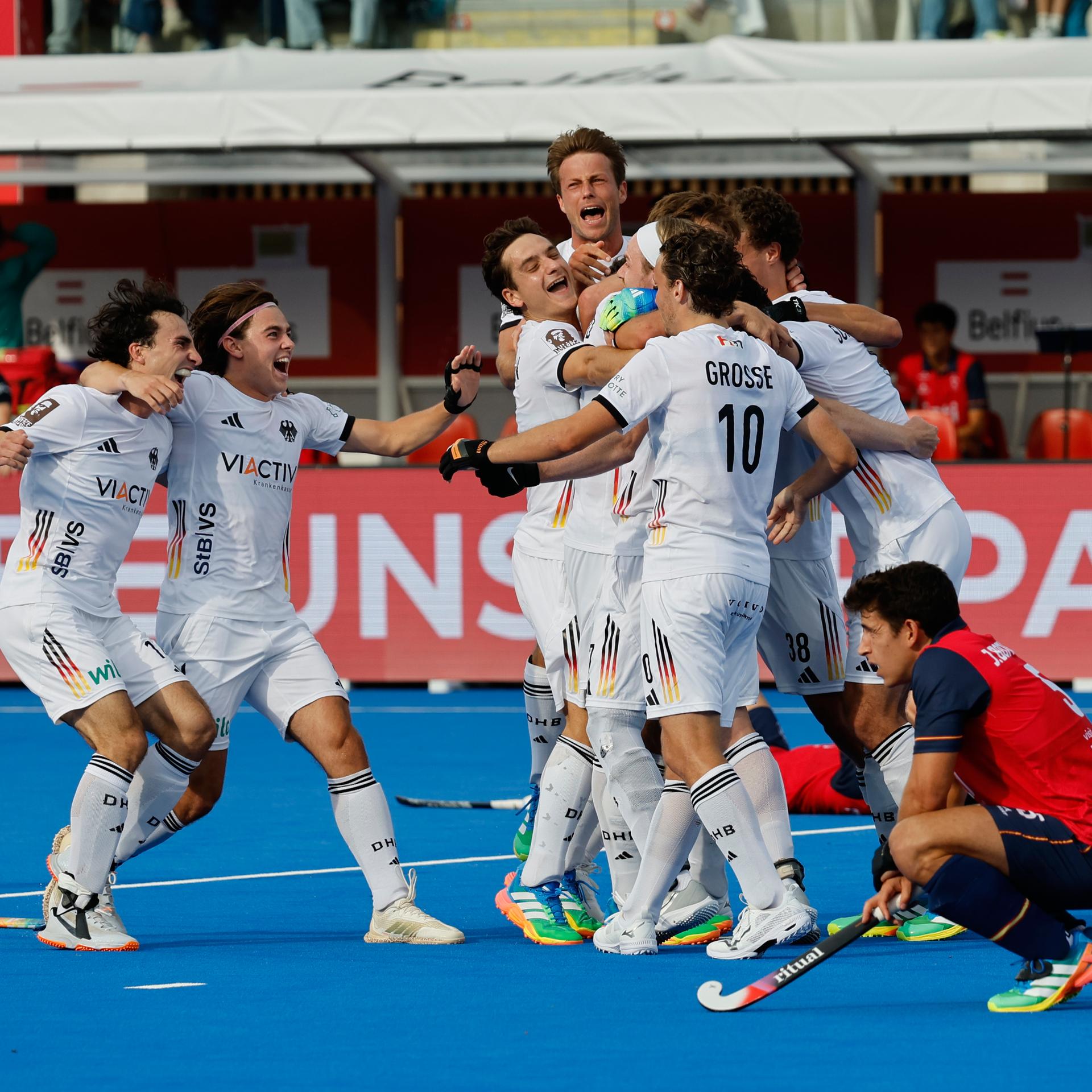 Deutsche Hockeyspieler sammeln sich zum Jubel und umarmen sich, im Vordergrund hockt ein spanischer Spieler niedergeschlagen am Boden.