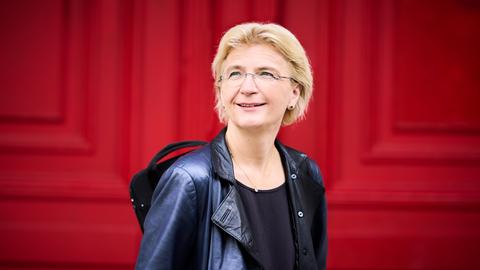 Antje Weithaas steht in Lederjacke und mit ihrem Geigenkoffer über der Schulter von einer knallroten Tür.