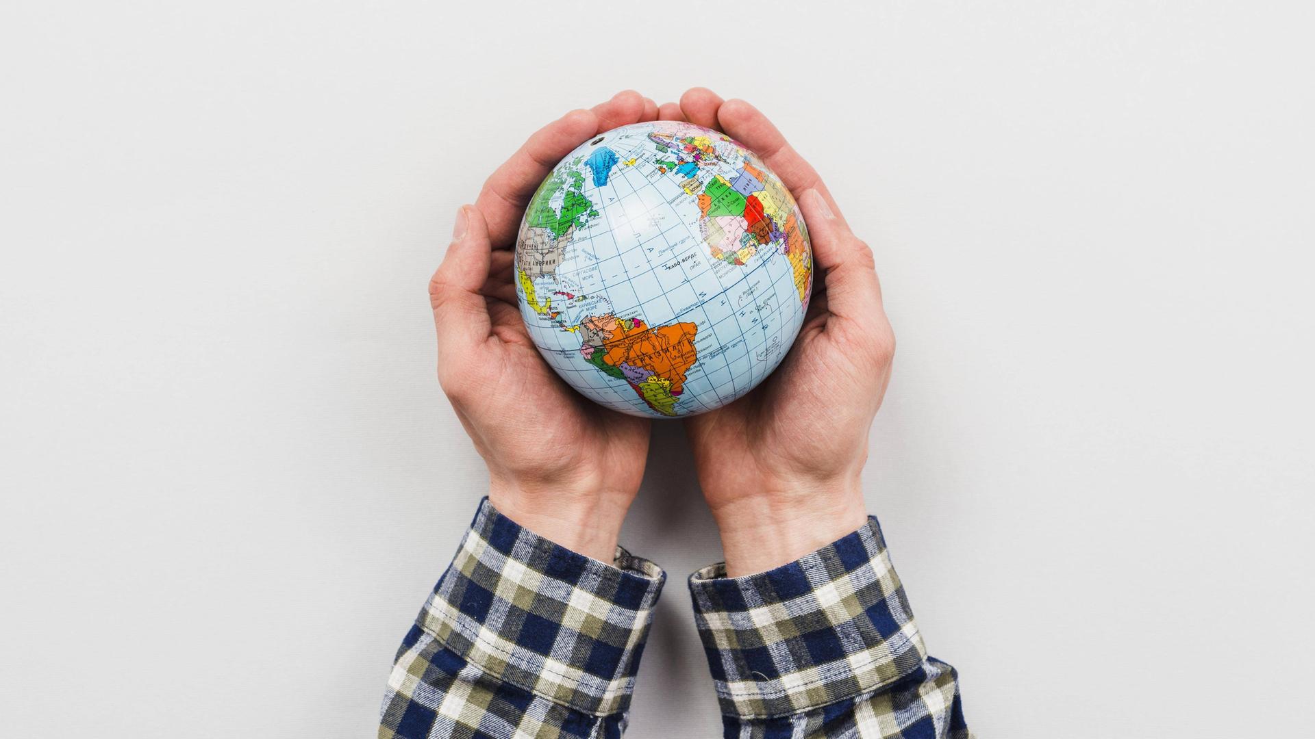 Zwei Hände halten einen Miniatur-Glous. Auf der sichtbaren Seite des Erdballs ist u.a. Südamerika zu sehen. 