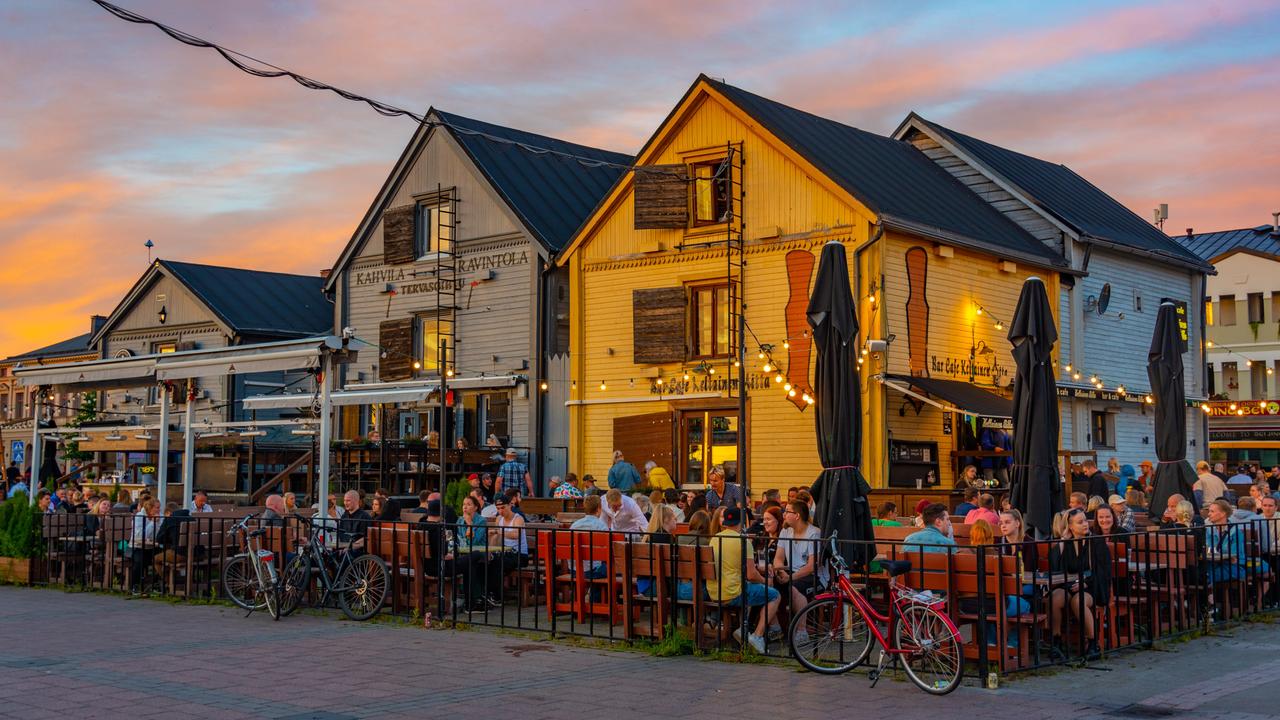 Vor bunten Holzhäuschen sitzen viele Menschen in einem Restaurantgarten.