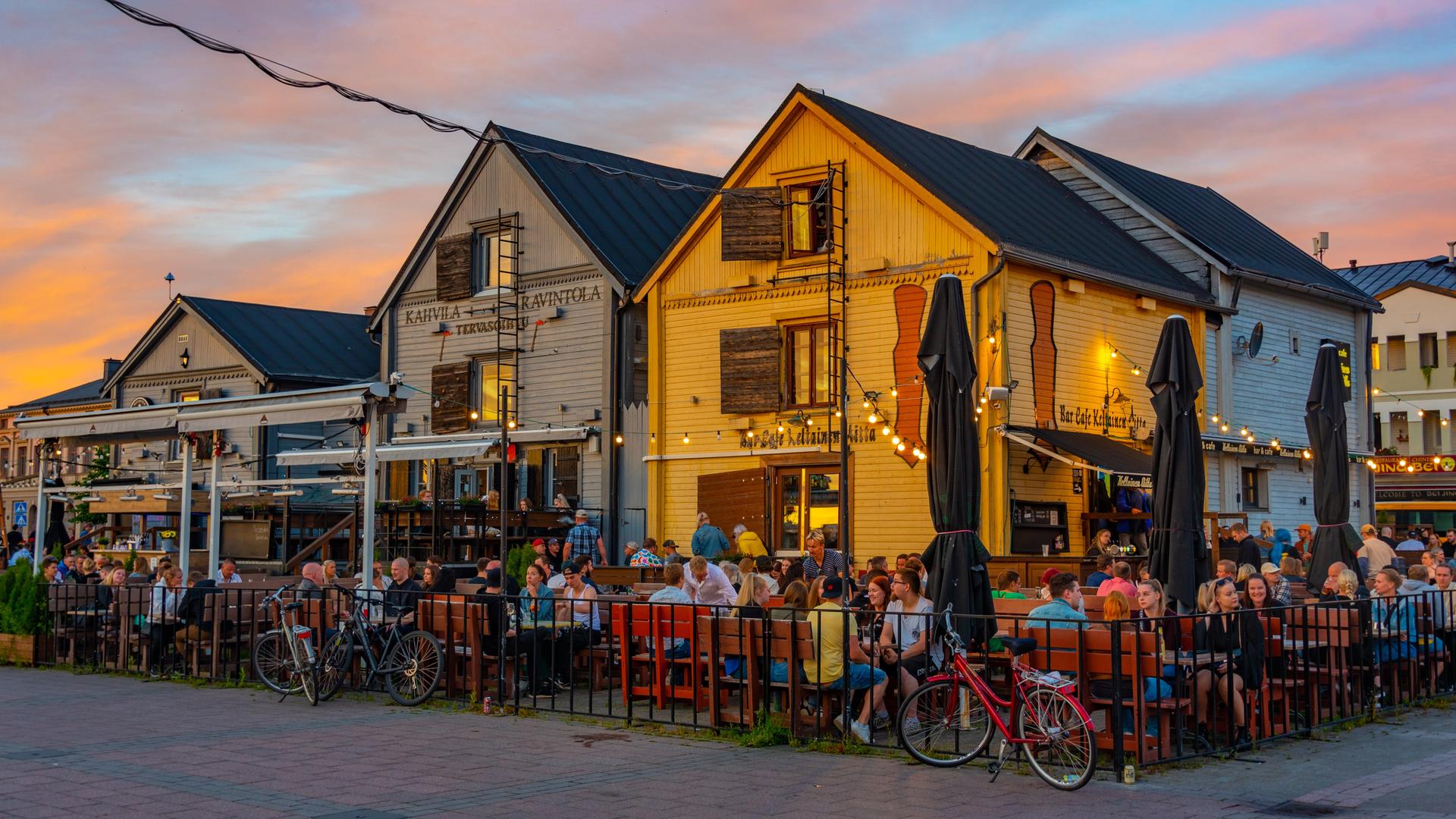 Vor bunten Holzhäuschen sitzen viele Menschen in einem Restaurantgarten.