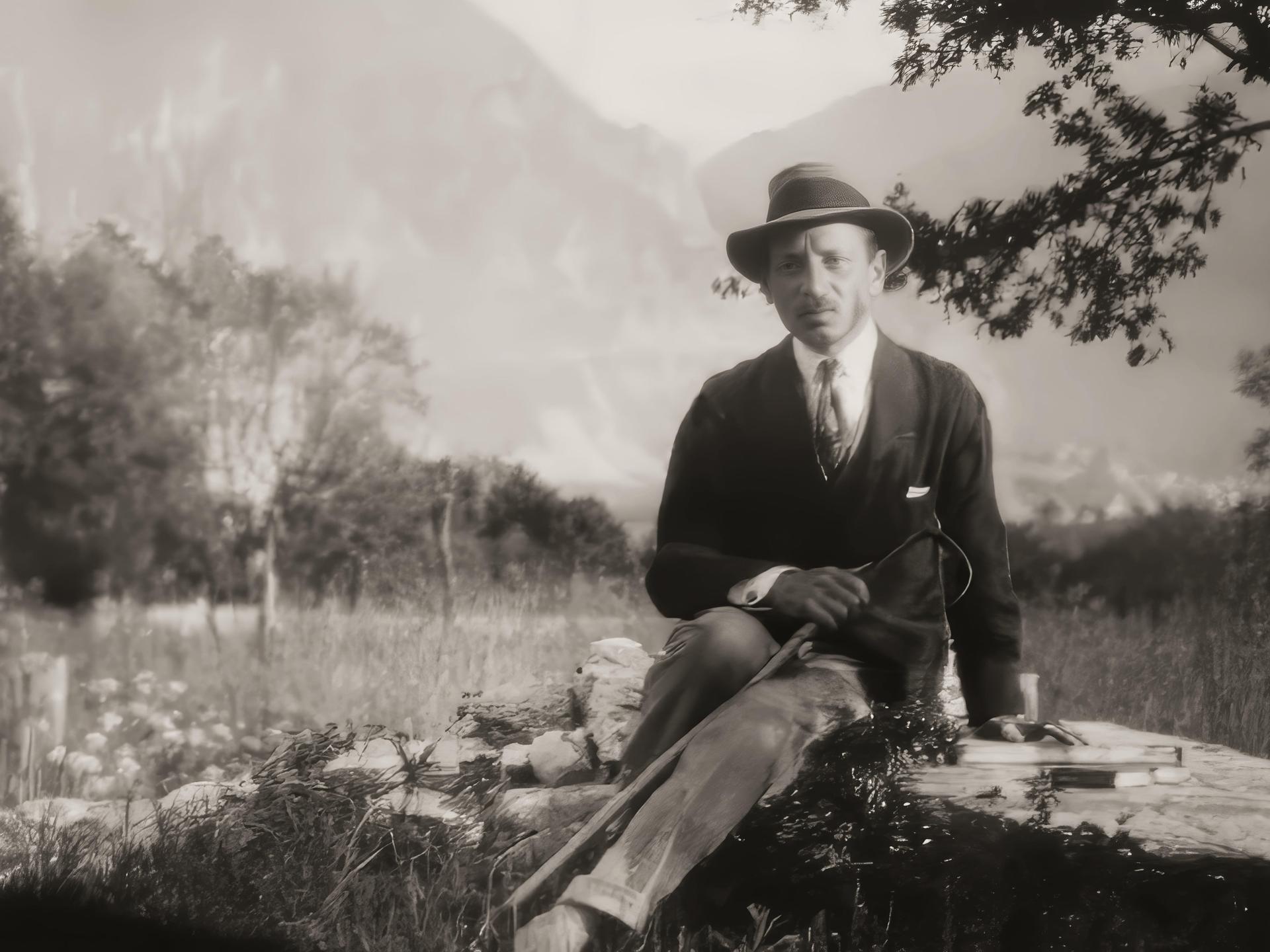 Rainer Maria Rilke auf einer historischen schwarz-weiß Aufnahme von 1924. Zu sehen ist eine Mann mit Stock und Hut auf einem Stein sitzend, neben ihm liegt ein Buch. Im Hintergrund schweizer Alpenpanorama von Château de Muzot.