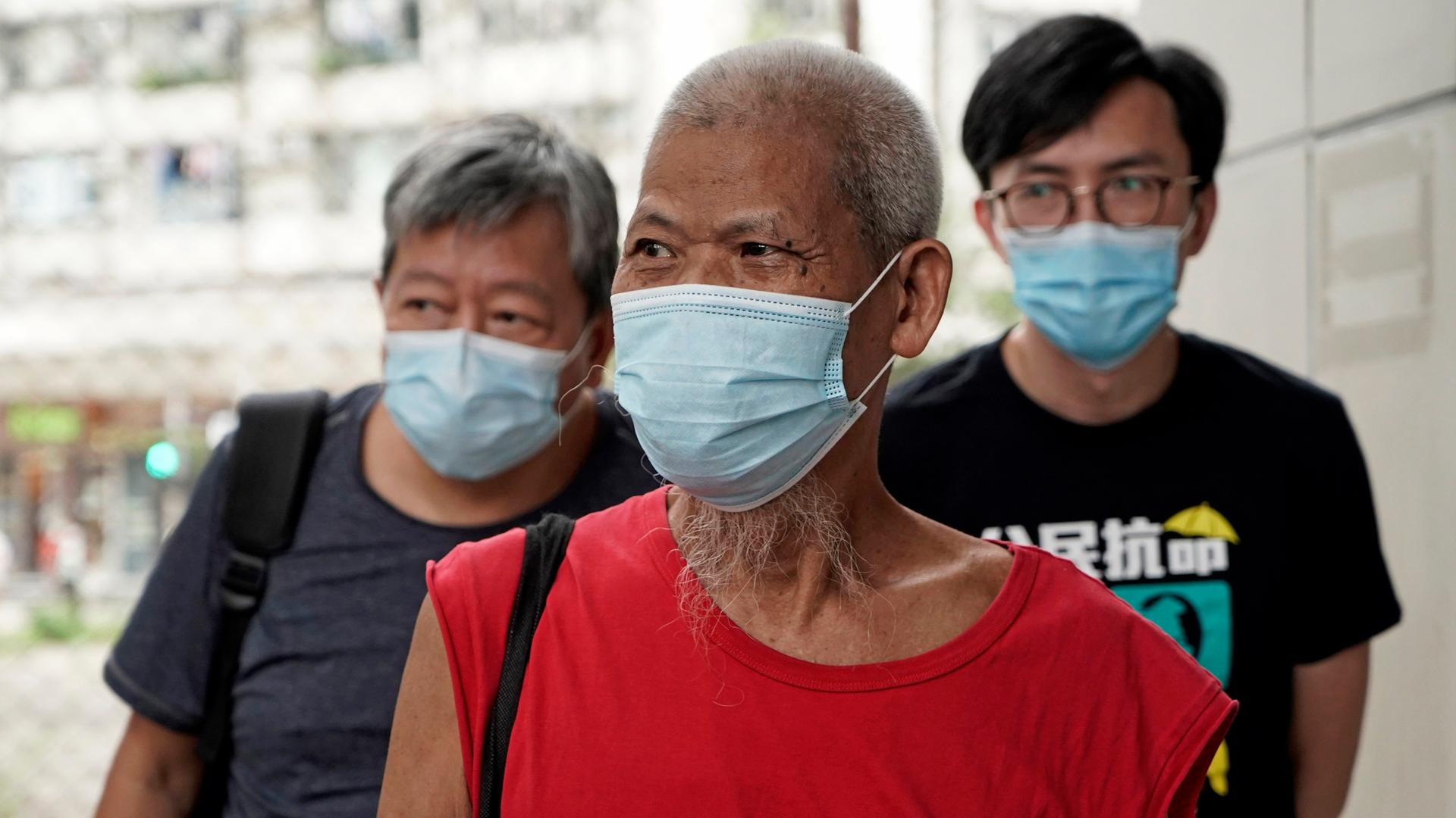 Der Hongkonger Demokratieaktivist Koo Sze Yiu in Begleitung von zwei Männern, sie alle tragen eine Maske.