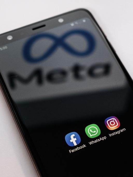 Auf einem Smartphone sind die Apps von Facebook, Whatsapp und Instagram zu sehen. Auf dem Bildschirm spiegelt sich der Schriftzug plus Logo von Meta.