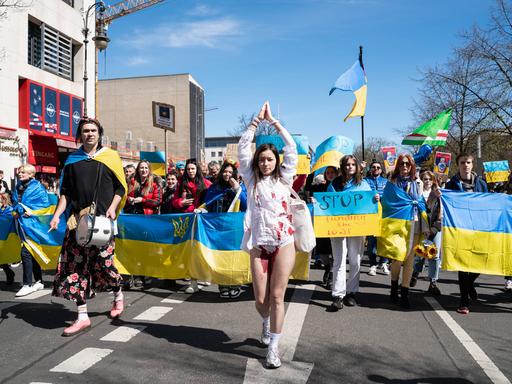Eine junge ukrainische Frau mit gefesselten Haenden und blutgetränktem Kleid führt eine Demonstration an.
