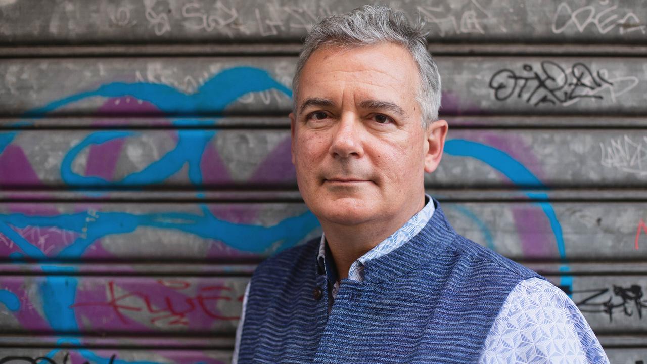 Ilija Trojanow steht für eine Porträtaufnahme vor dem verschlossenen Tor einer Garage, auf dem sich Graffiti befinden