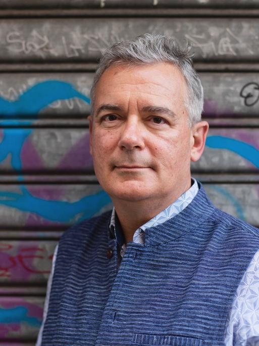 Ilija Trojanow steht für eine Porträtaufnahme vor dem verschlossenen Tor einer Garage, auf dem sich Graffiti befinden Ilija Trojanow steht für eine Porträtaufnahme vor dem verschlossenen Tor einer Garage, auf dem sich Graffiti befinden