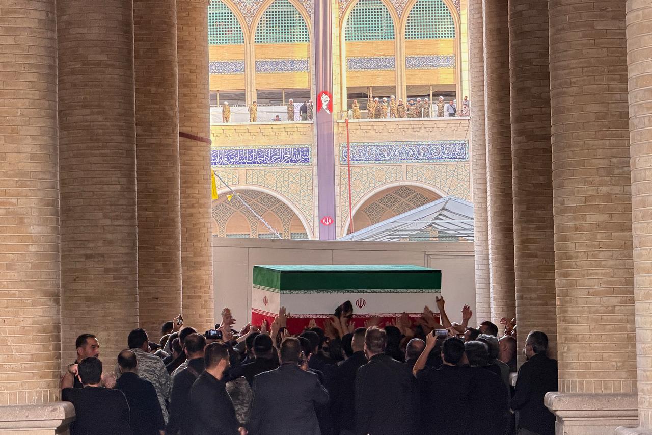 Das Bild zeigt eine Menschenmenge, die einen Sarg in den Farben der iranischen Flagge trägt. Im Hintergrund sind Teile der Mosalla-Moschee in Teheran zu sehen.