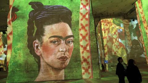 In einem dunklen Raum sind Gemälde an die Wand projeziert. Darunter ist auch ein Selbstporträt der mexikanischen Künstlerin Frida Kahlo. In einem dunklen Raum sind Gemälde an die Wand projeziert. Darunter ist auch ein Selbstporträt der mexikanischen Künstlerin Frida Kahlo.