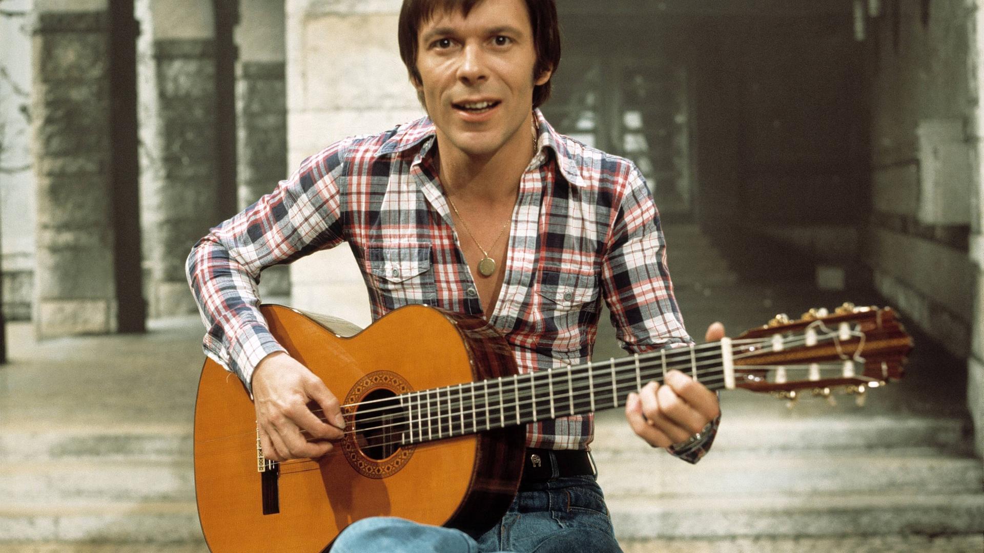 Mey sitzt mit einer Gitarre in den Händen auf einem Hocker.