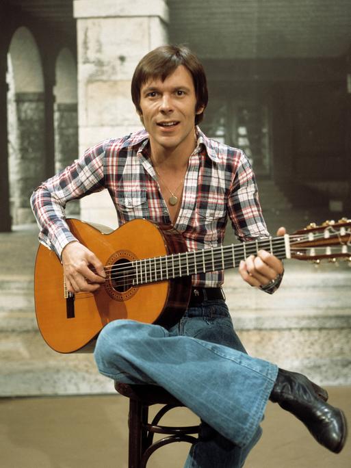 Mey sitzt mit einer Gitarre in den Händen auf einem Hocker.