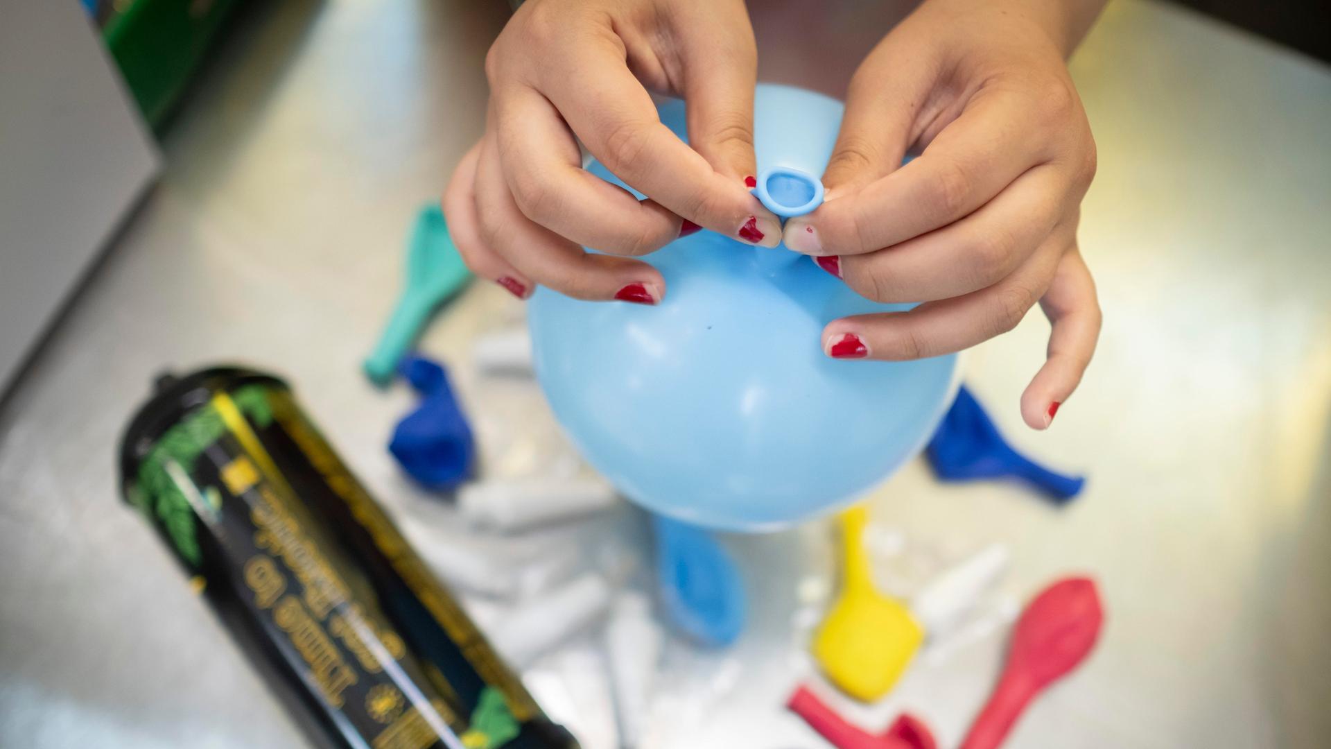 Zwei Hände halten einen Luftballon gefüllt mit Lachgas über einen Lachgasbehälter. Die Hände sehen jung aus. Auf den Fingernägeln ist absplitternder roter Nagellack. Zwei Hände halten einen Luftballon gefüllt mit Lachgas über einen Lachgasbehälter. Die Hände sehen jung aus. Auf den Fingernägeln ist absplitternder roter Nagellack.