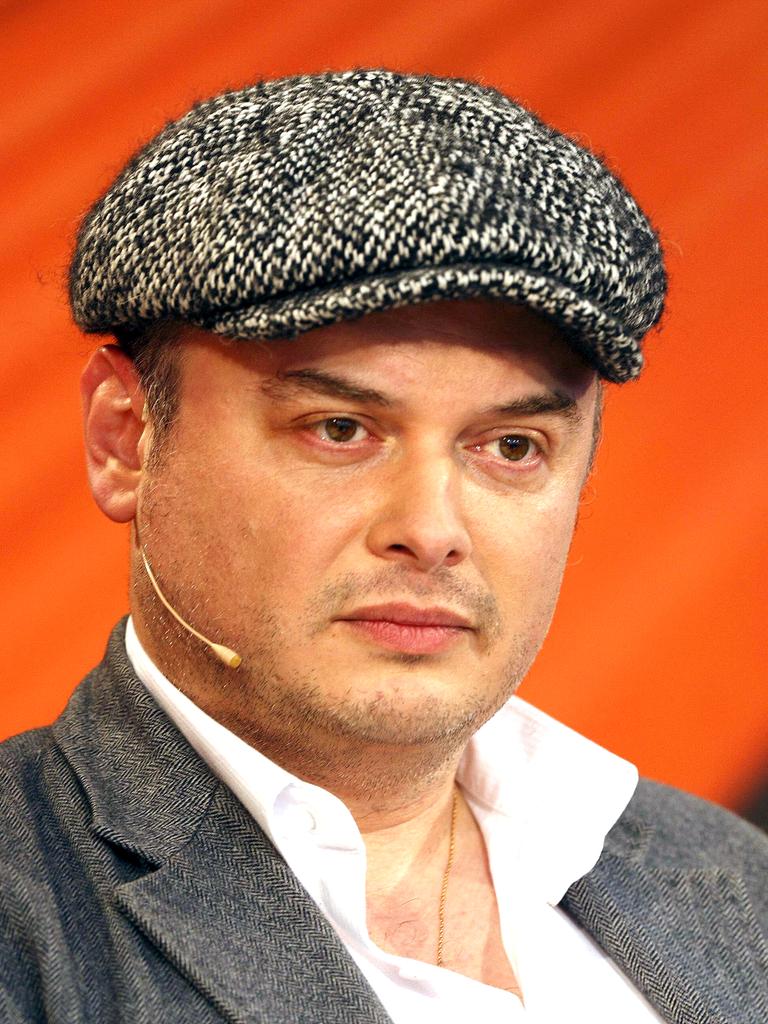 Der Schriftsteller und Psychologe Catalin Dorian Florescu mit weißem Hemd, grauer Jacke und einer Mütze mit Hahnentritt-Muster sitzt vor einem orangenen Hintergrund und scheint konzentriert zuzuhören.
