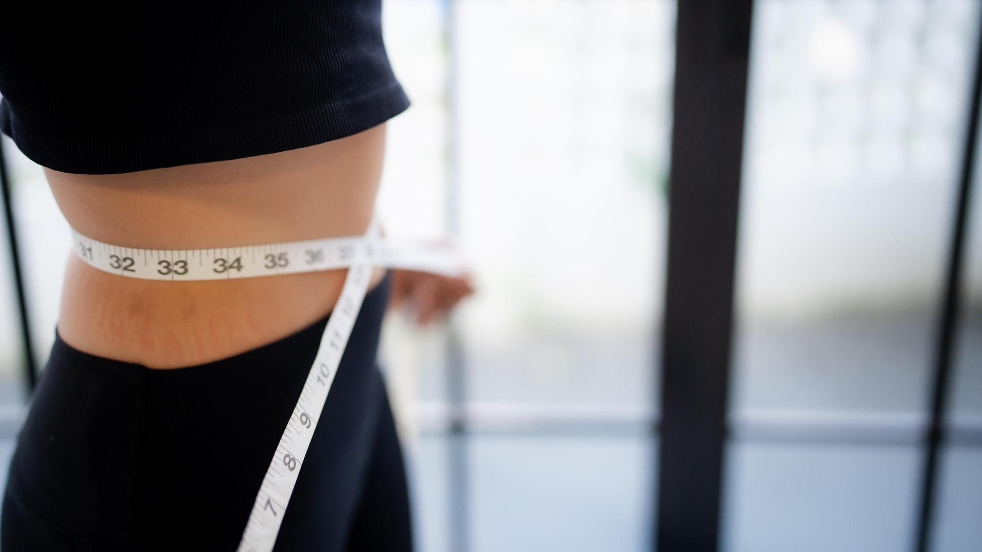 Eine Frau misst ihre Taille mit einem Maßband