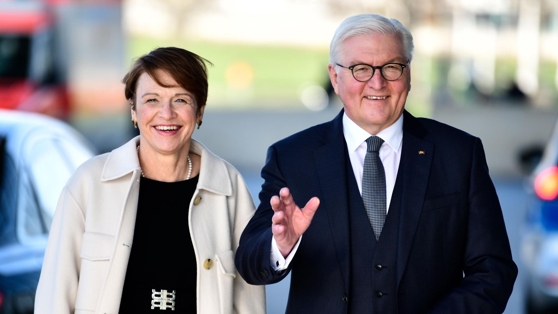 Bundespräsident Frank-Walter Steinmeier und seine Frau Elke Büdenbender gehen auf einer Straße frontal auf eine Fotokamera zu und winken freundlich. Aufnahme vom 14.03.2022.