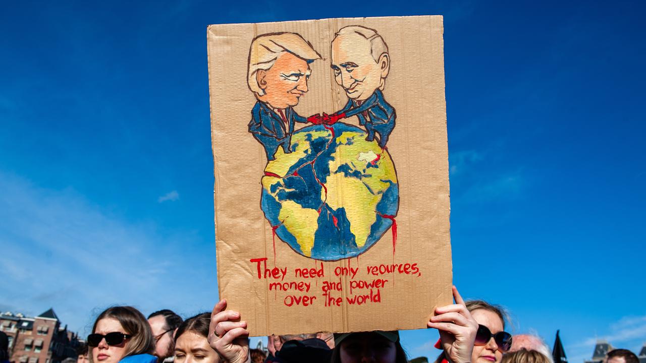 Eine Demonstrantin hält ein Pappschild mit einer Illustration von Wladimir Putin und Donald Trump, die die Welt unter sich aufteilen