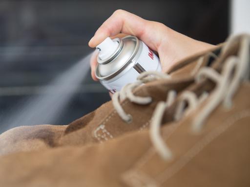 Eine Frau sprüht Imprägnierspray auf Lederschuhe.