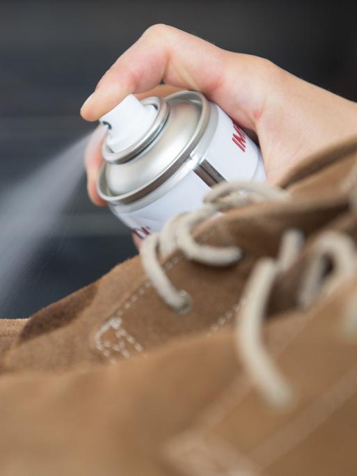 Eine Frau sprüht Imprägnierspray auf Lederschuhe. Eine Frau sprüht Imprägnierspray auf Lederschuhe.