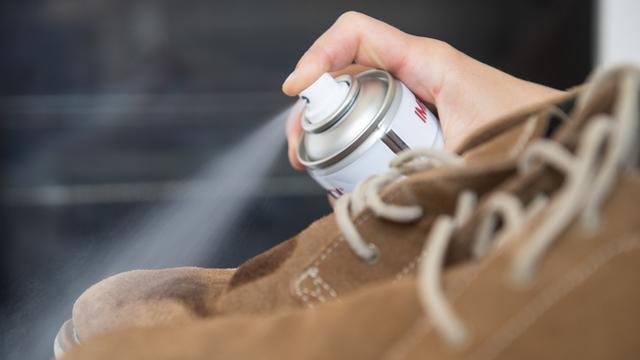 Eine Frau sprüht Imprägnierspray auf Lederschuhe.