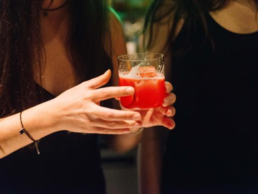 Nahaufnahme einer Frau, die ein Lowballglas mit einem roten Drink in der Hand hält.