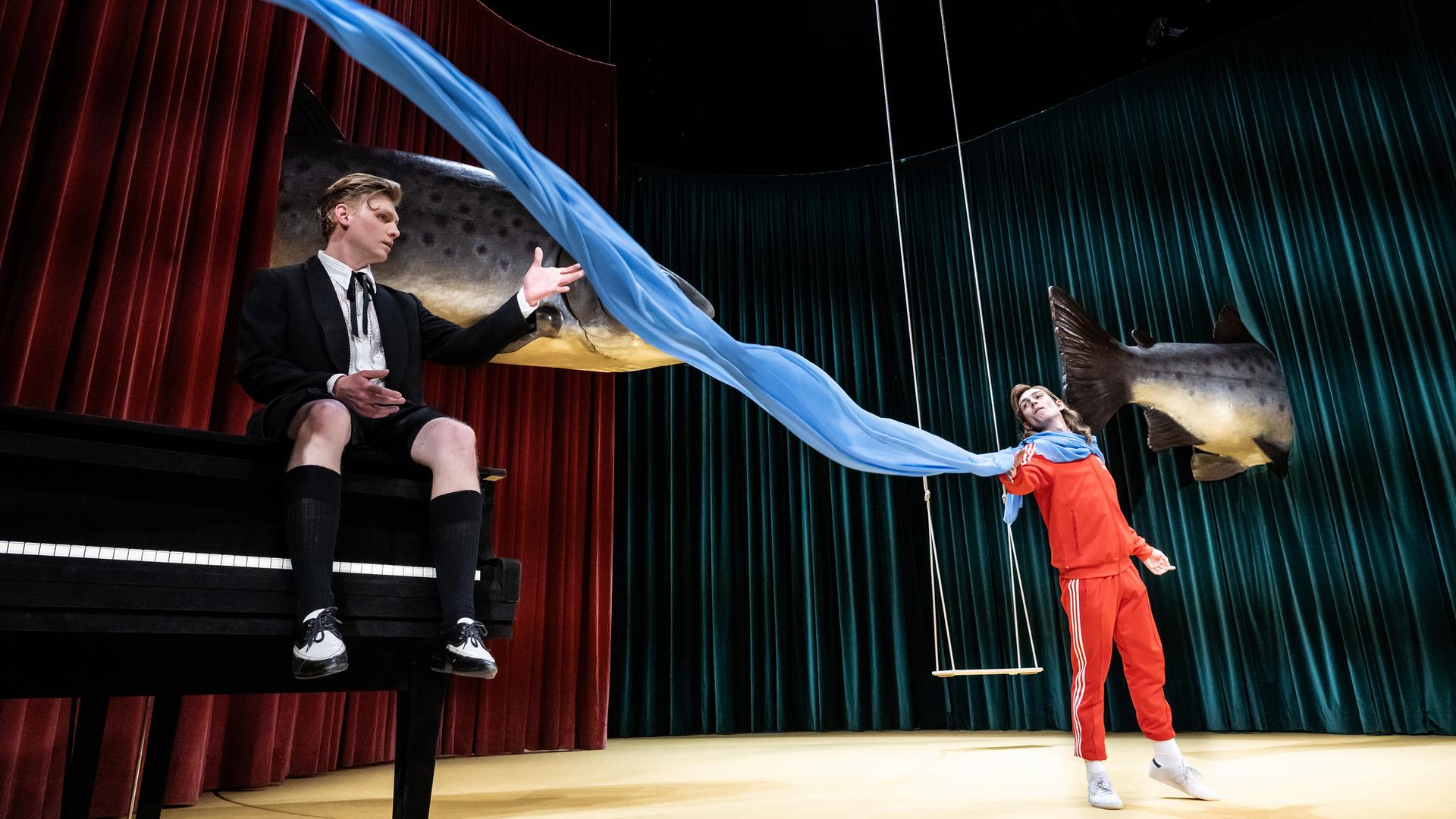 Zwischen den Schauspielern Johannes Nussbaum und Vincent zur Linden flattert ein blaues Tusch quer über die Bühne. Im Hintergrund schweben zwei riesige Fische.