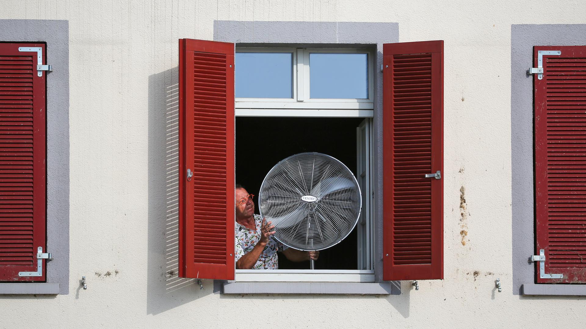 Ein Mann stellt am Morgen einen Ventilator an sein geöffnetes Fenster.
