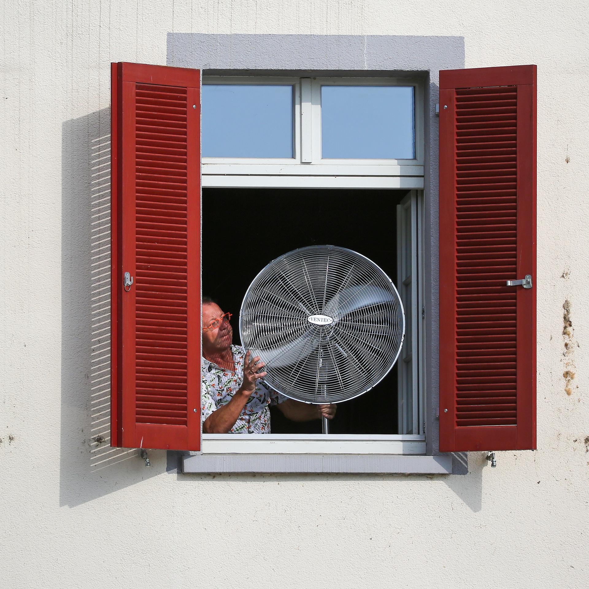 Ein Mann stellt am Morgen einen Ventilator an sein geöffnetes Fenster.