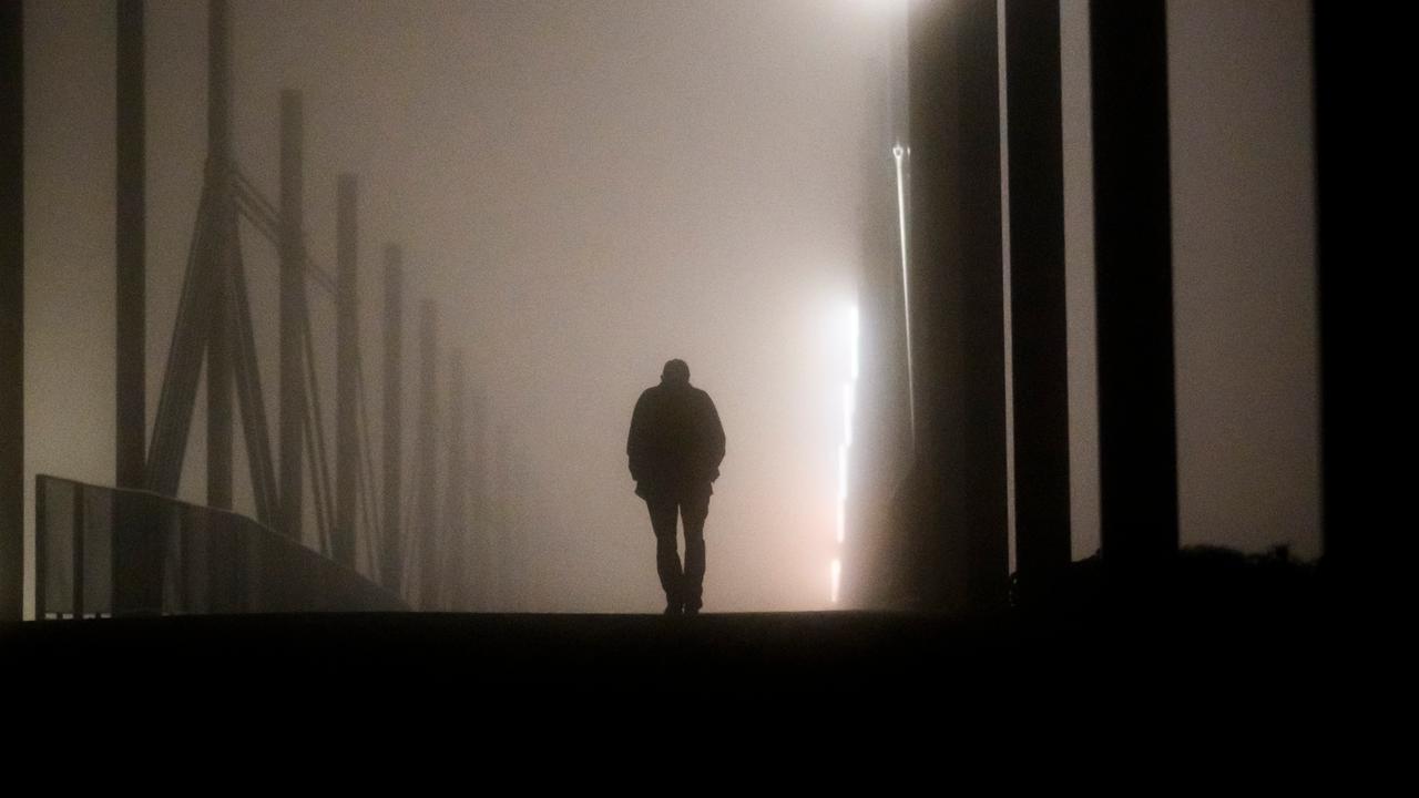 Ein Mann geht am frühen Morgen bei Nebel über eine Brücke.