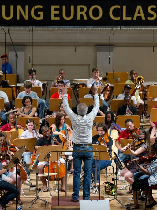 Ein Mann mit grauem Haar dirigiert das Miagi Youth Orchestra während einer Probe.