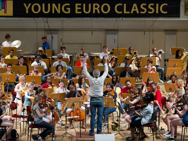 Ein Mann mit grauem Haar dirigiert das Miagi Youth Orchestra während einer Probe.