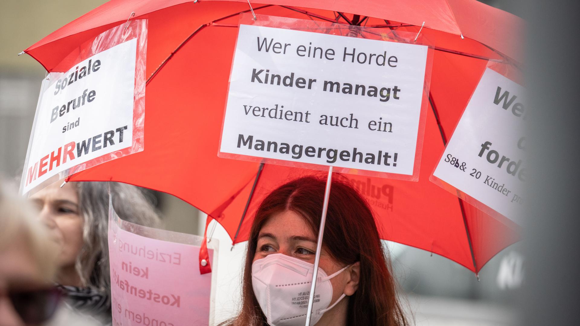 Eine Demonstrantin trägt bei einem Protestmarsch einen Regenschirm mit einem Plakat und der Aufschrift "Wer eine Horde Kinder managt, verdient auch ein Managergehalt". Eine Demonstrantin trägt bei einem Protestmarsch einen Regenschirm mit einem Plakat und der Aufschrift "Wer eine Horde Kinder managt, verdient auch ein Managergehalt".