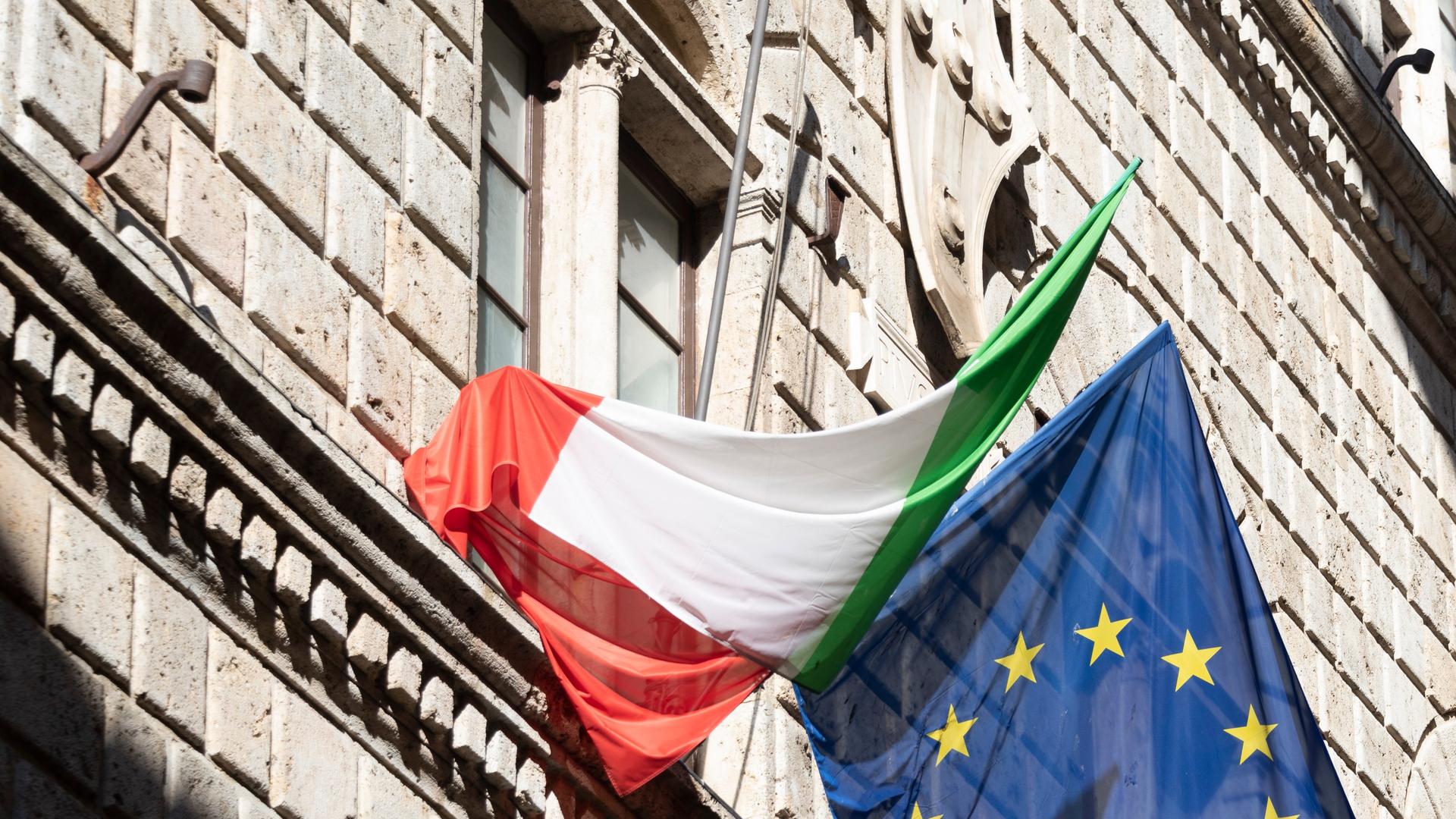 Eine italienische und eine europäische Flagge hängen an einer Hausfassade in Siena