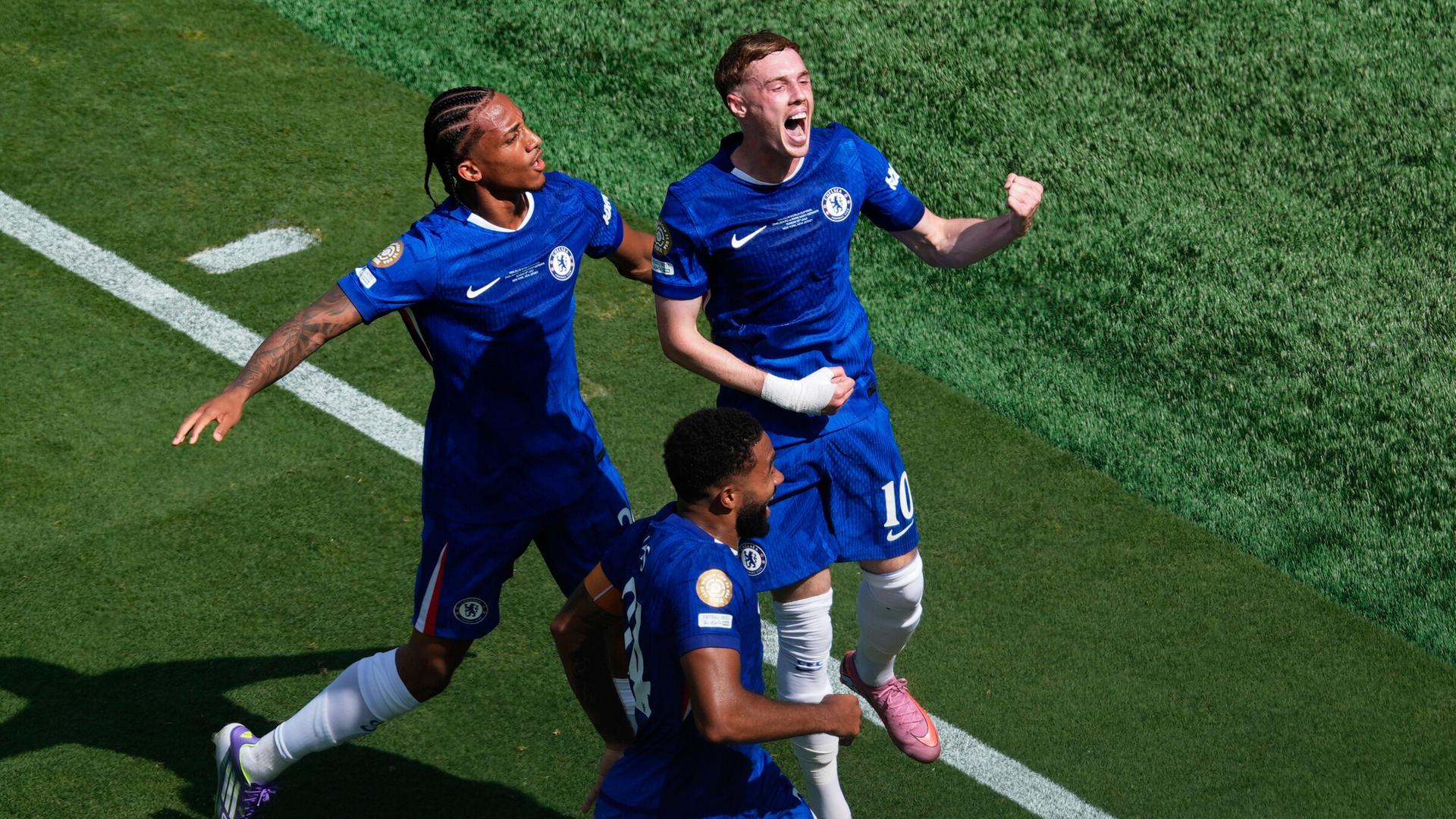 Das Bild zeigt den jubelnden Fußballspieler Cole Palmer, der von zwei Mitspielern umgeben ist. Das Bild zeigt den jubelnden Fußballspieler Cole Palmer, der von zwei Mitspielern umgeben ist.